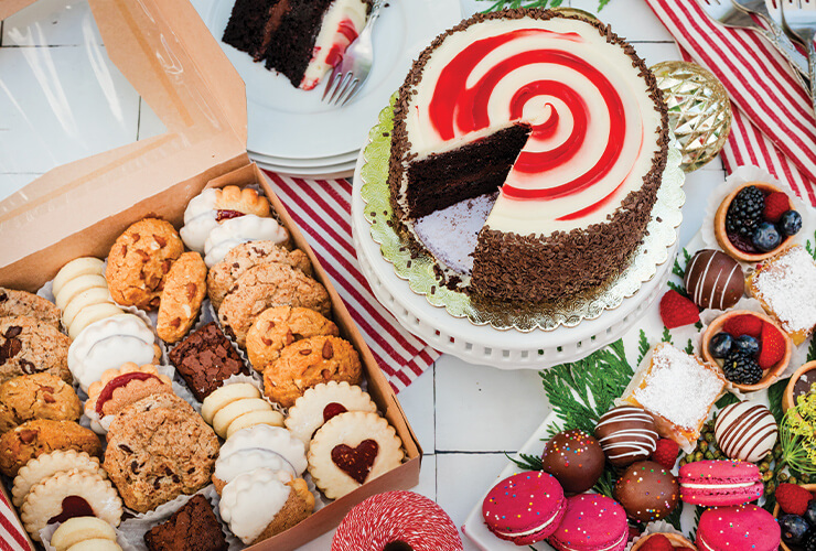 a table with a peppermint chocolate cake, a box of cookies and a tray of mini desserts.