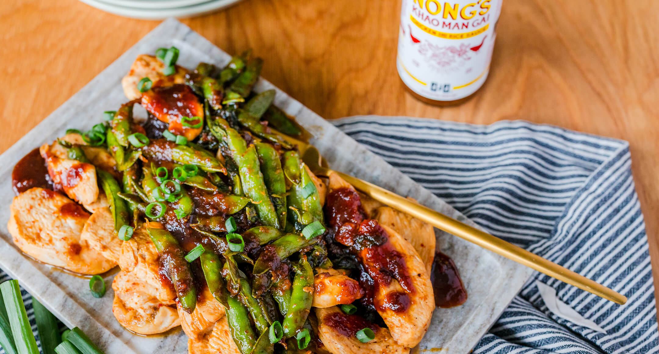 A plated dish of stir-fried chicken with snap peas featuring Nong's Khao Man Gai Sauce.