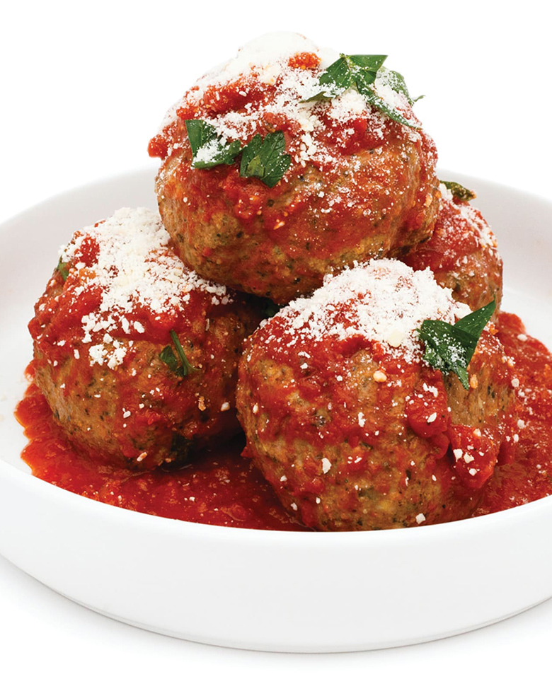 meatballs in sauce piled in a white bowl and topped with parmesan cheese.