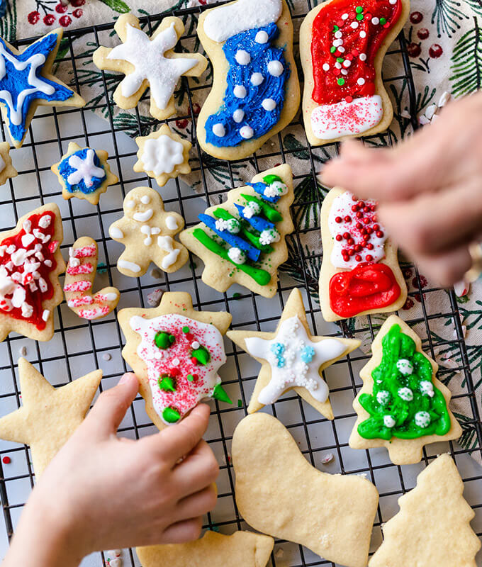 an overhead shot of hands with sugar coookies on a cooling rack wiht some decorated and others plain