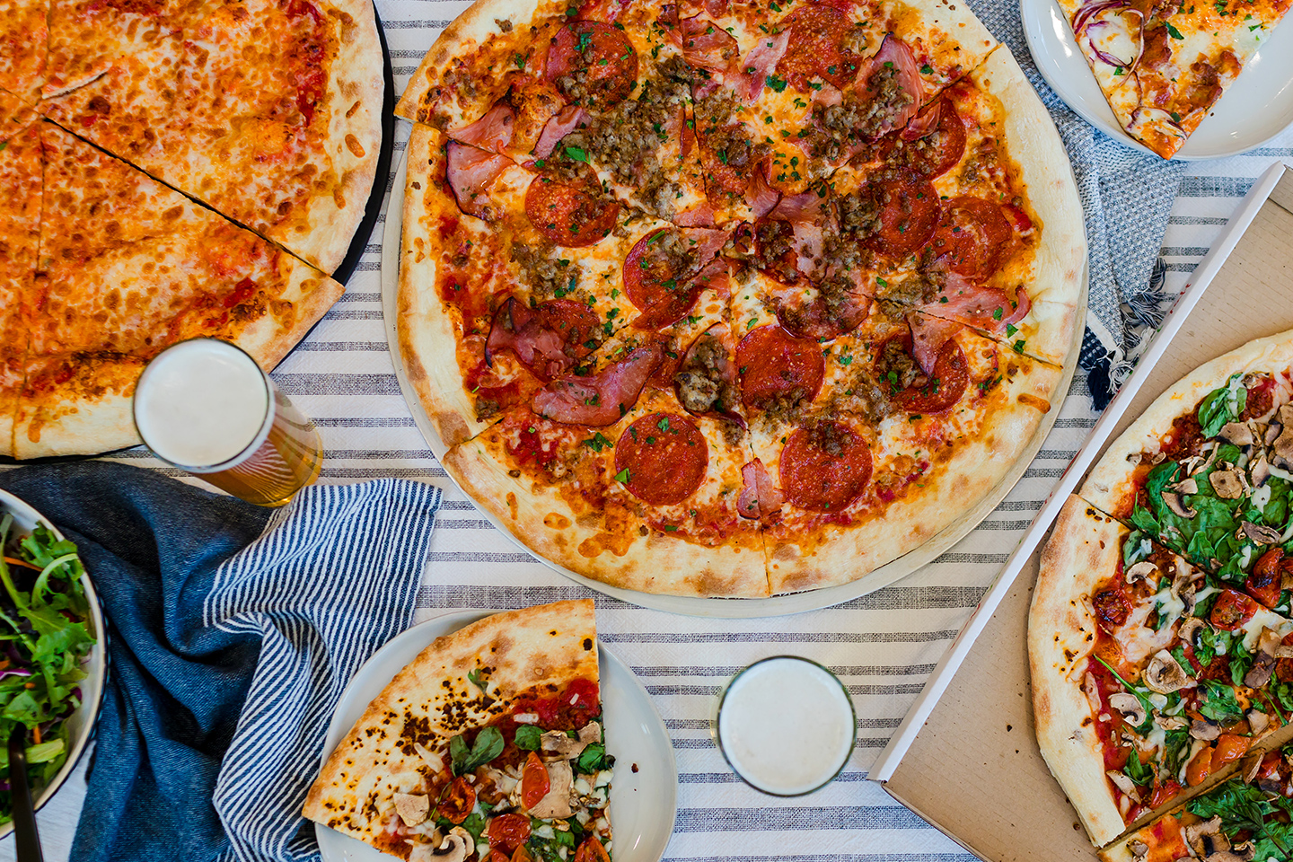 A table topped with freshly baked pizza and pints of beer.
