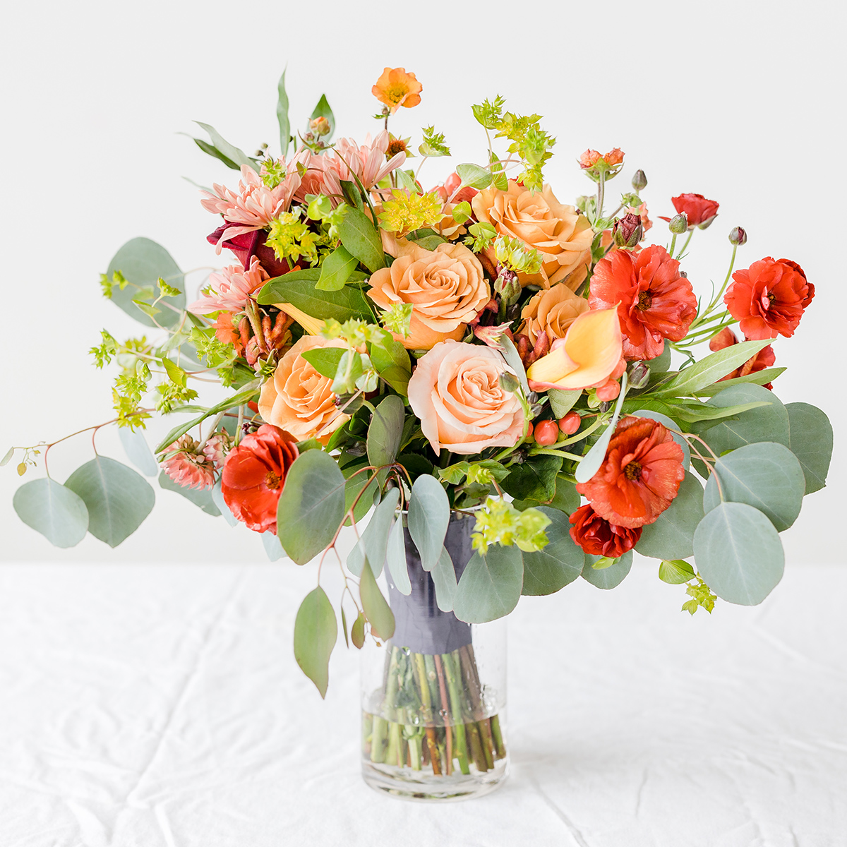 Bouquet of coral and red florals in a tall glass vase