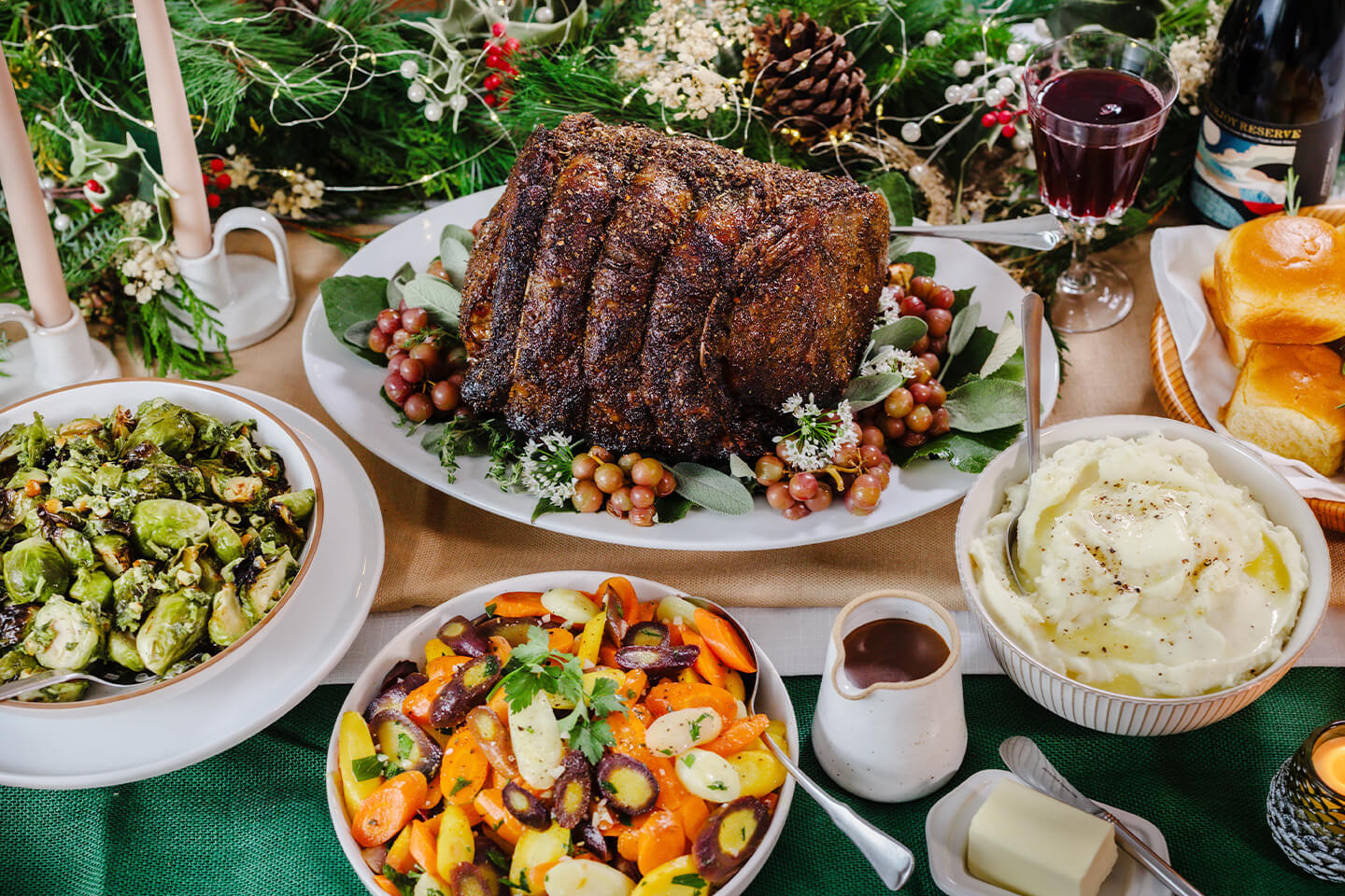 A table spread of rib roast, mashed potatoes, gravy, carrots, Brussels sprouts and rolls.