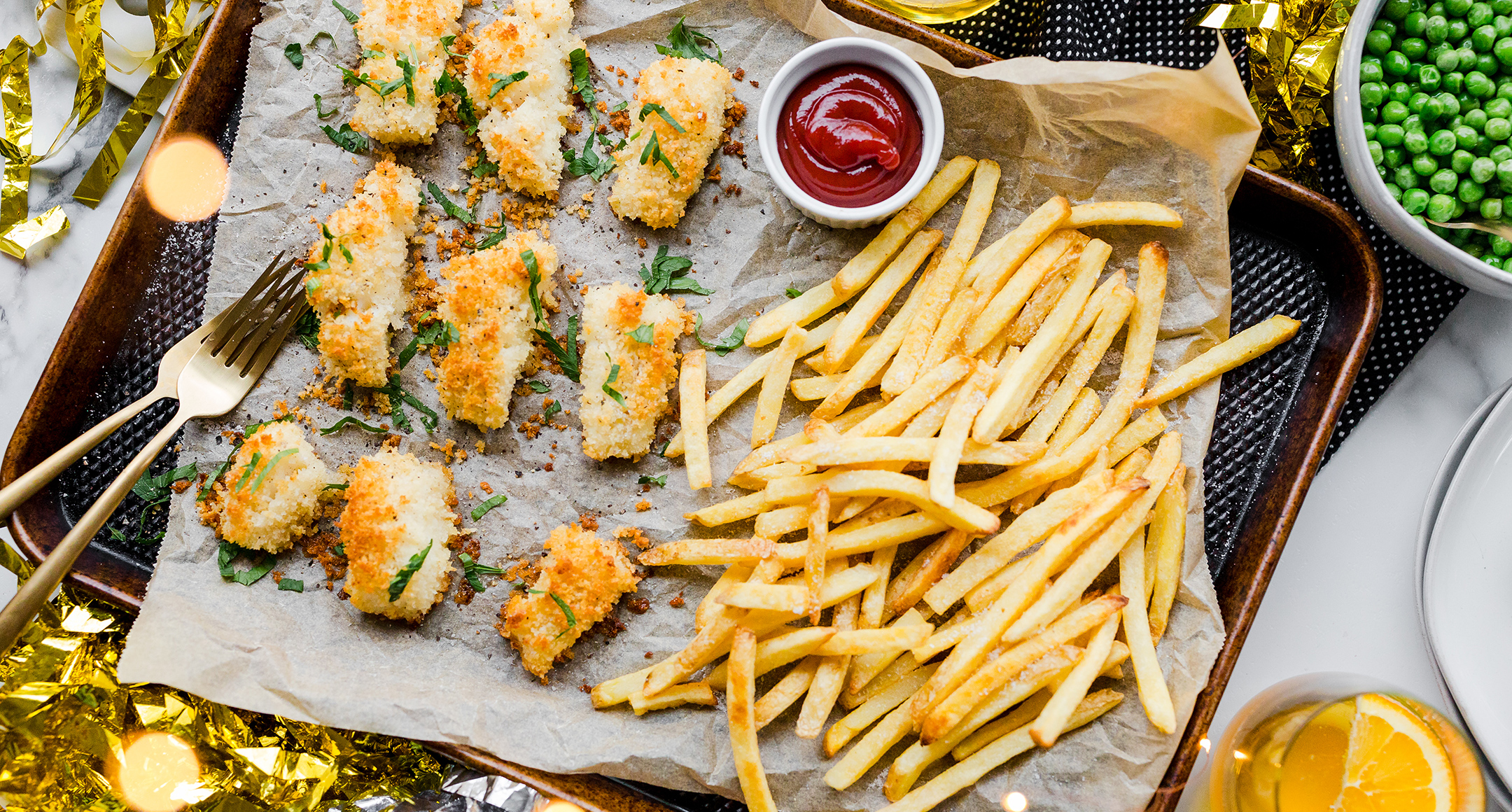 A sheet pan filled with breaded and baked cod fillets with a side of French fries.