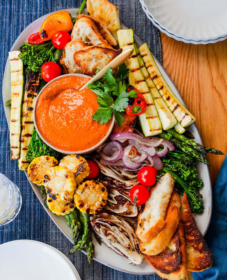 Romesco Dip on a platter with grilled zucchini, bread, corn, peppers, and onions