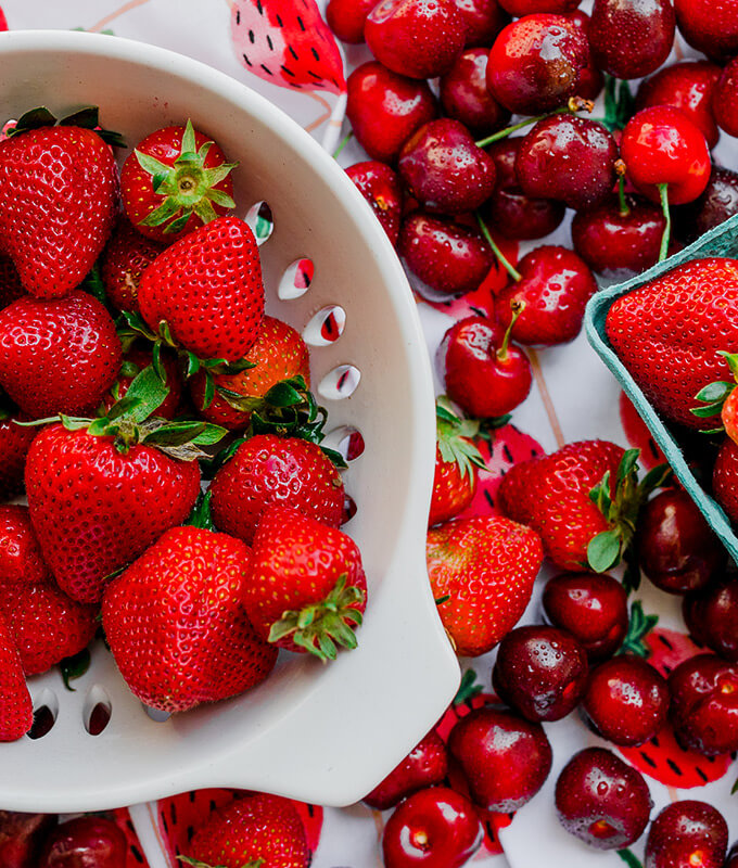 fresh red strawberries and cherries in a colander and on a counter top