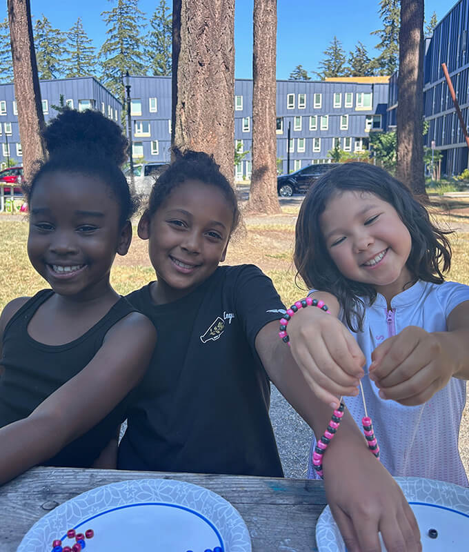 three young girls sitting at a table outside and smiling for the camera.