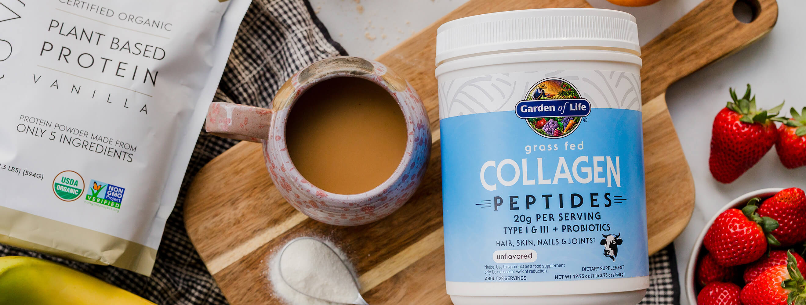 An overhead shot of packaged collagen and protein powder on a kitchen counter top with fruit and a mug with a beverage.