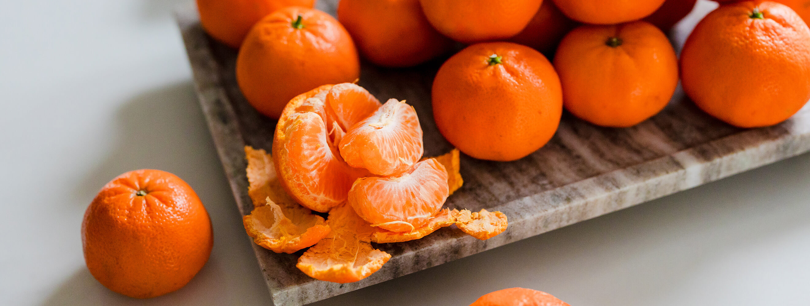 fresh satsuma mandarin oranges on a platter with one peeled open