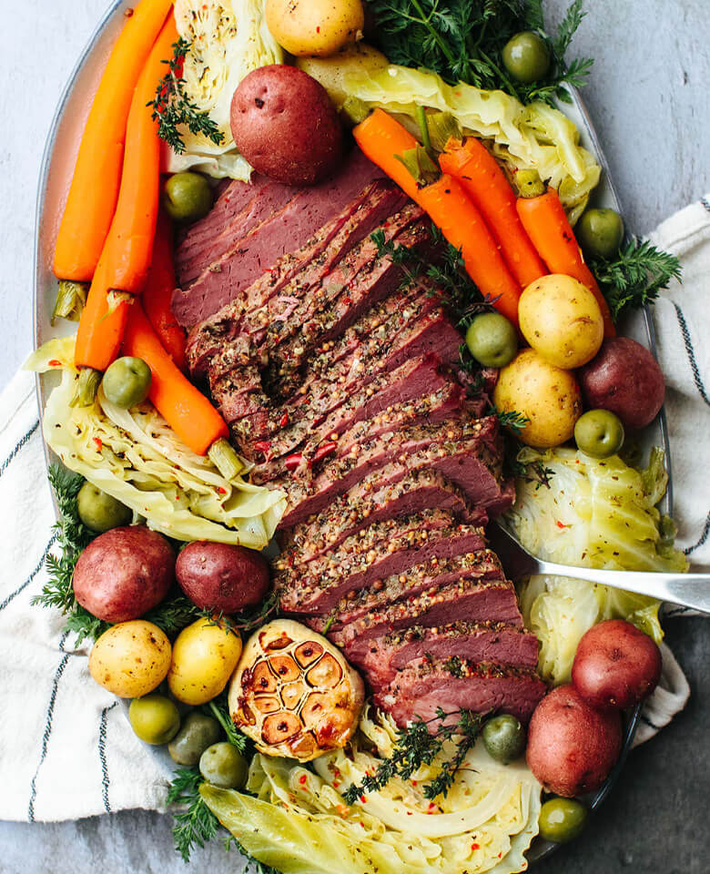 A slided corned beef on a platter with carrots, potatoes and cabbage.
