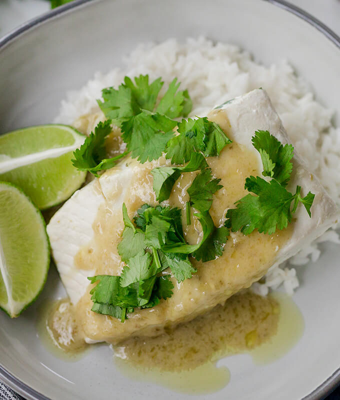 a piece of halibut fish on a plate with a green sauce, limes and white rice.