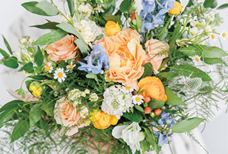 A natural bouquet of seasonal dainty yellow, blue, and orange flowers mixed with leafy tendrils.