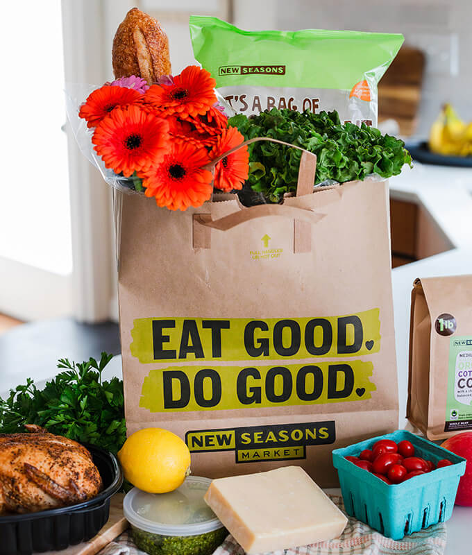 a bag of groceries on a counter with fresh food surround it like strawberries and chicken.