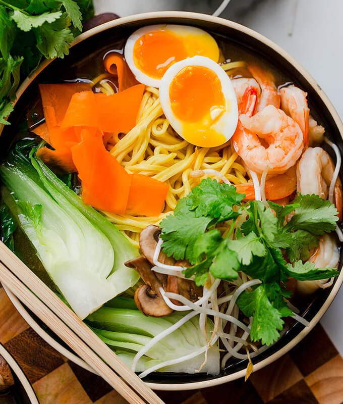 a bowl of ramen with bok choy, herbs, egg, shrimp and noodles in broth