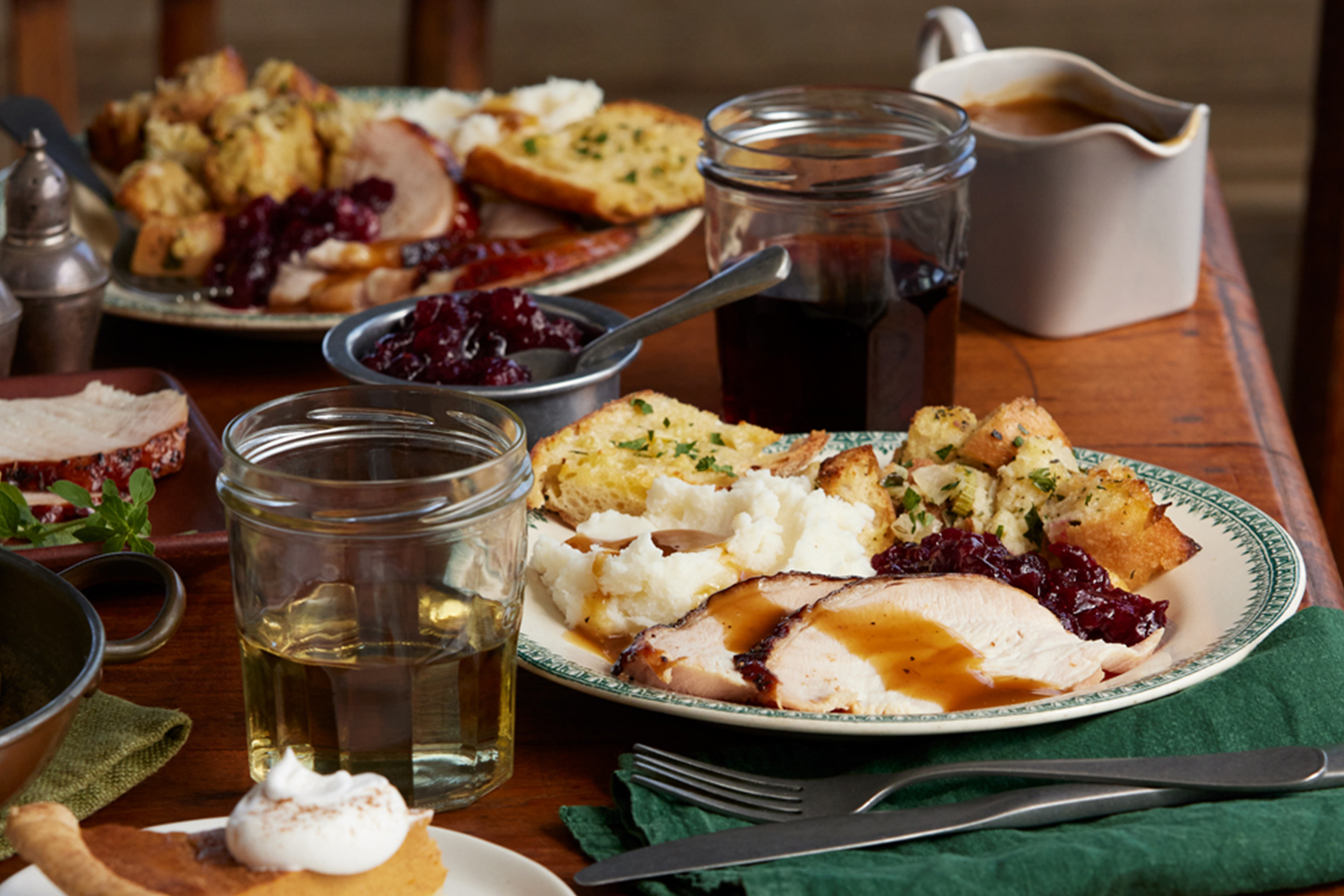 A festive holiday table with plates of sliced turkey, bread stuffing, mashed potatoes, and gravy.