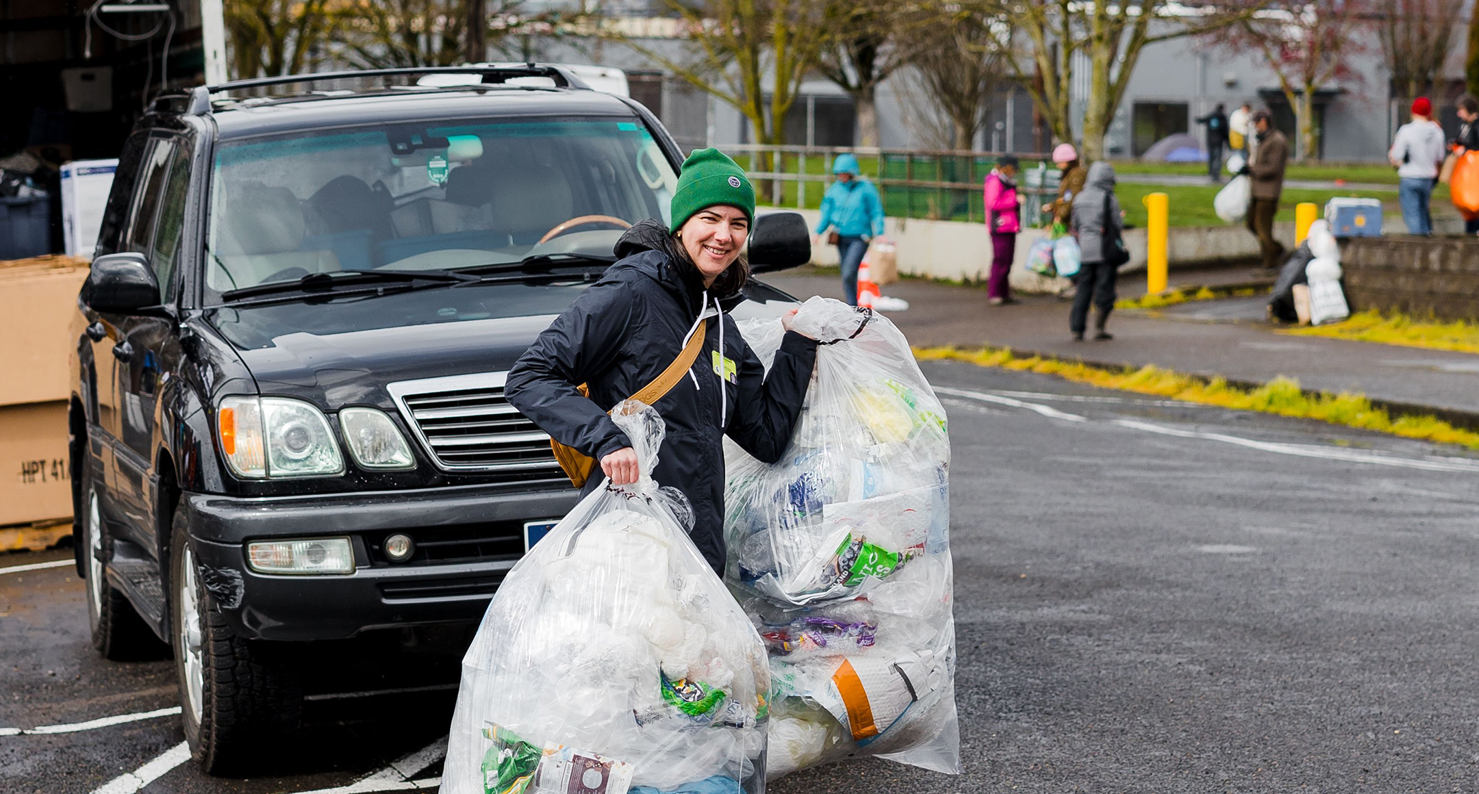 New Seasons Senior Manager of Sustainability, Athena Petty, shown carrying two large bags of recyclables across a parking lot. 