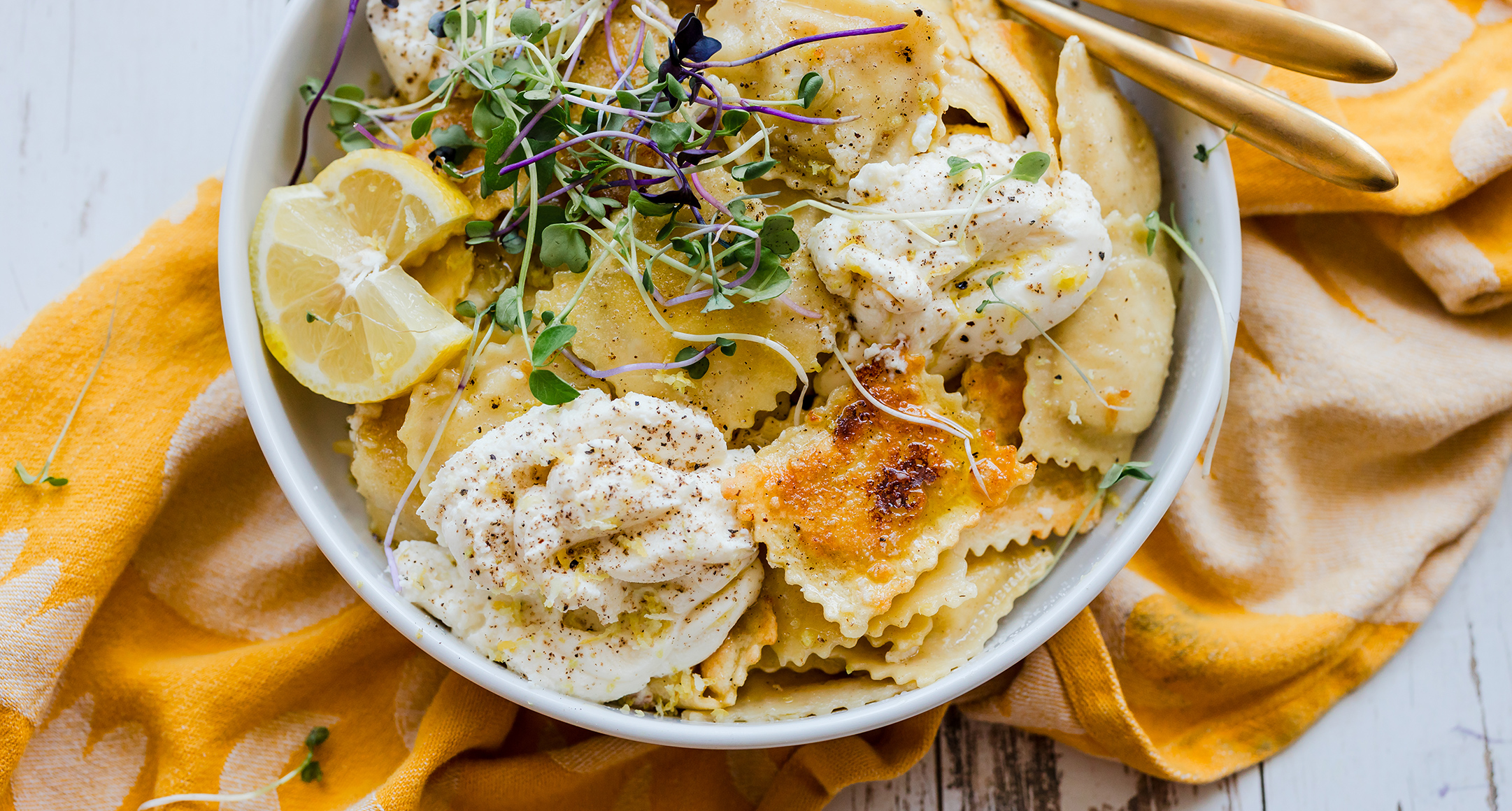 fresh ravioli with microgreens and lemon in a white bowl on a yellow towel