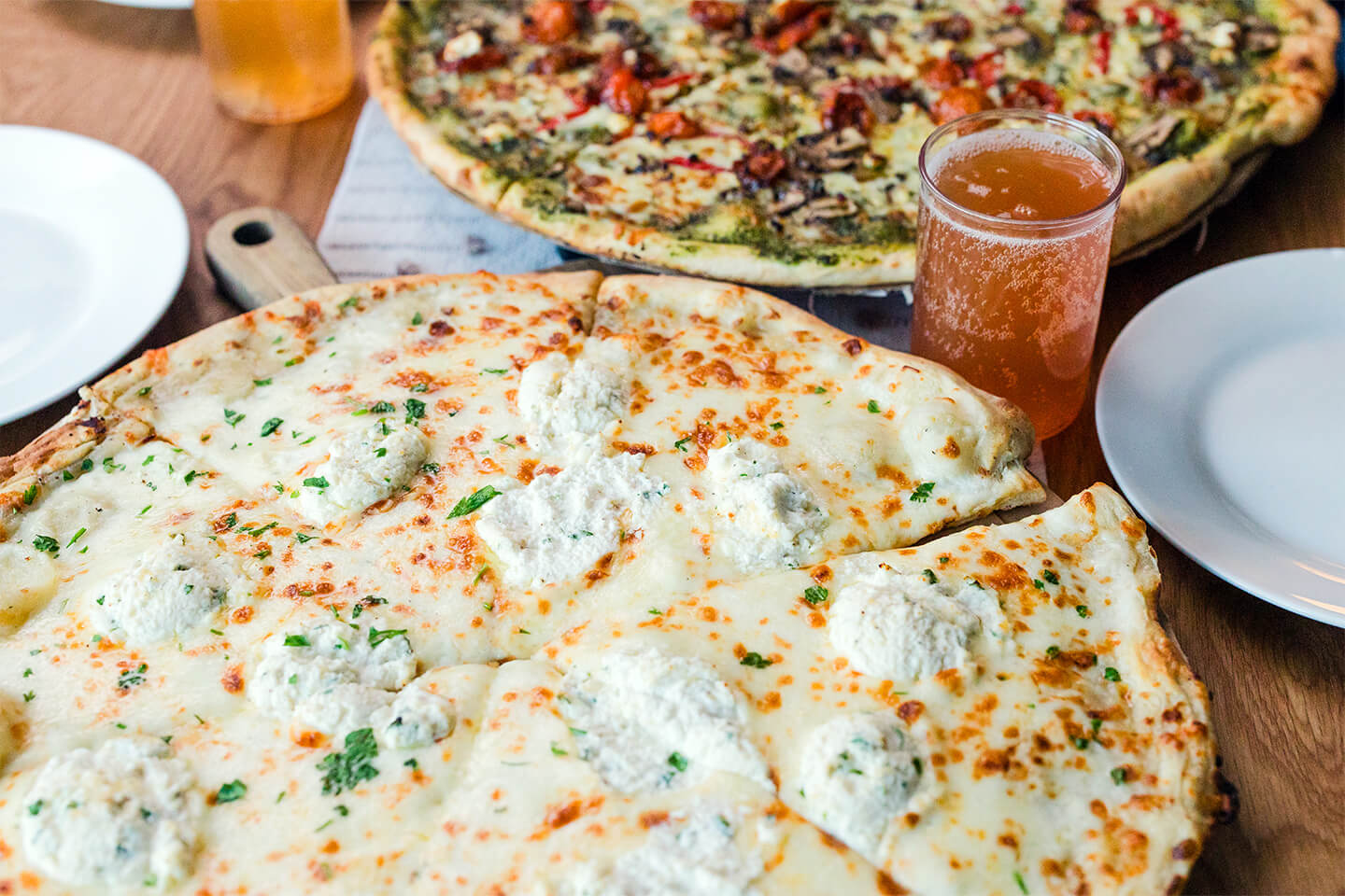 Picnic setting featuring a whole pizza, side salad, beer, and slice of pizza on a plate.