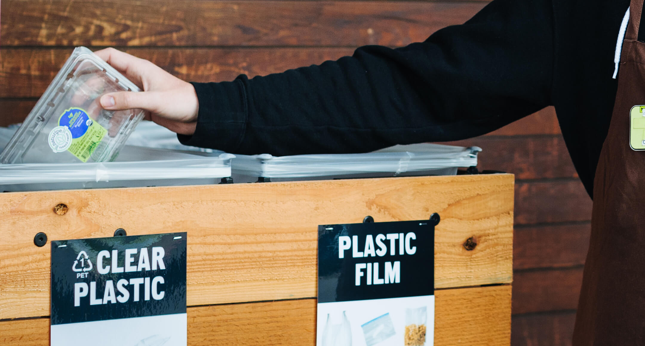 An image showing an individual placing an empty plastic container in a designated recycling bin.