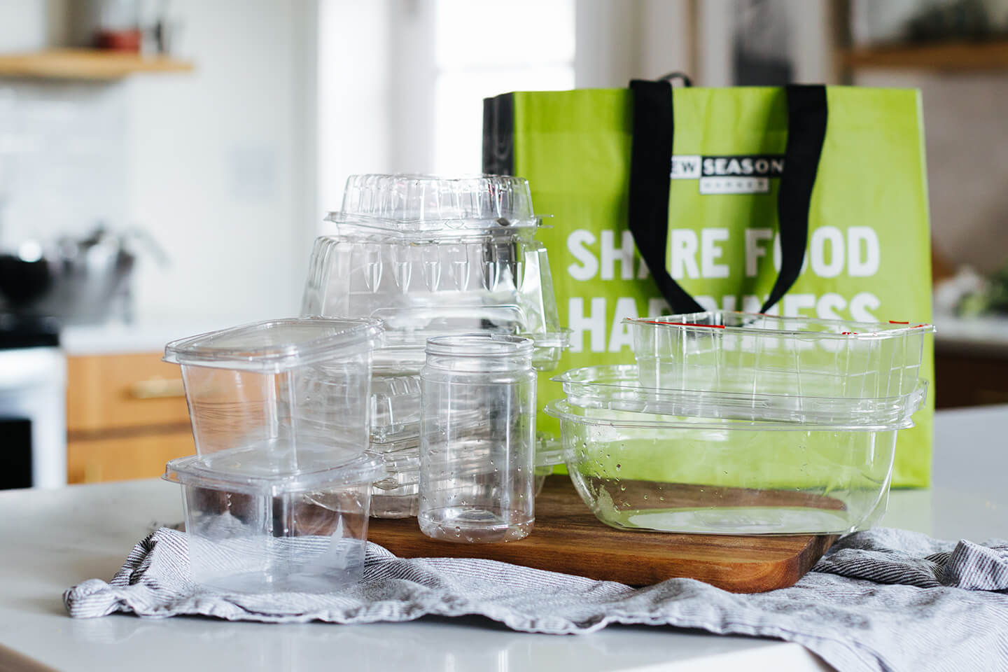 Various clean plastic containers on a counter top sitting in front of a reusable shopping bag.