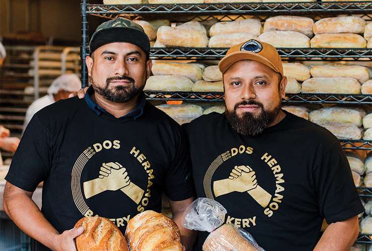 Two Dos Hermanos team members in bakery holding product.