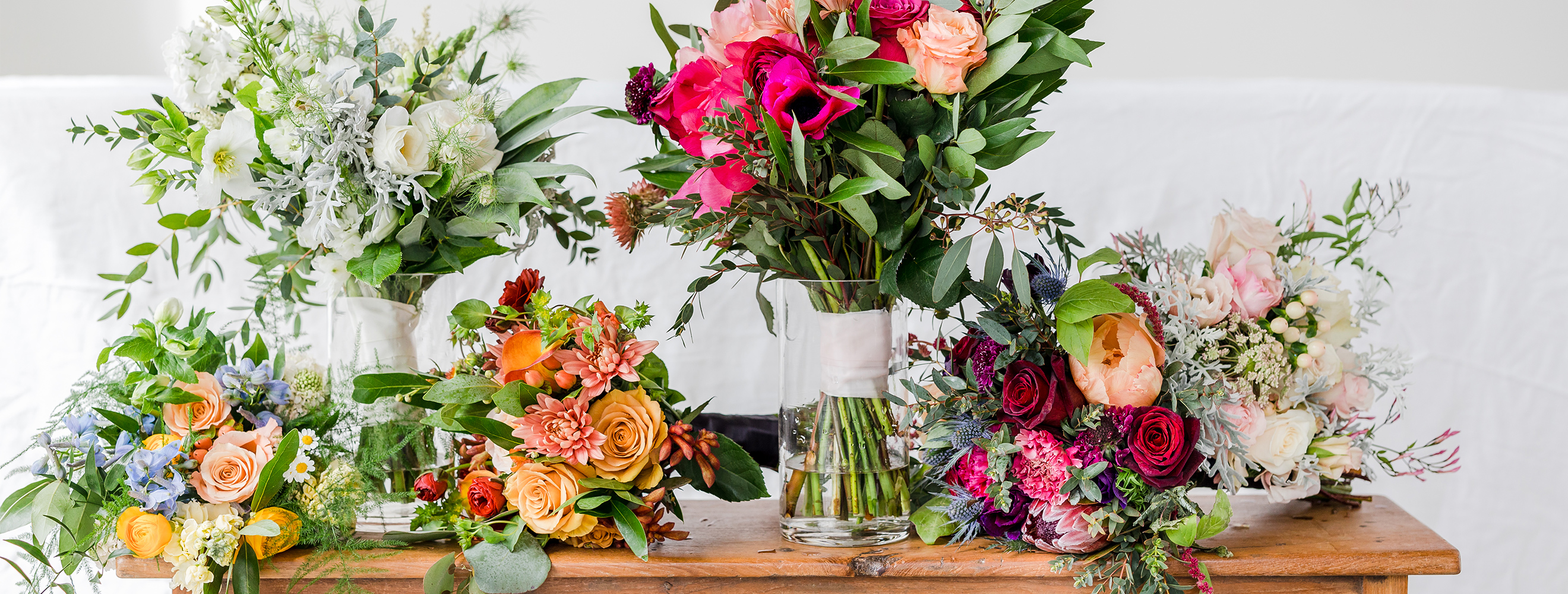 Five wedding bouquets of colorful flowers sit atop a wooden table.
