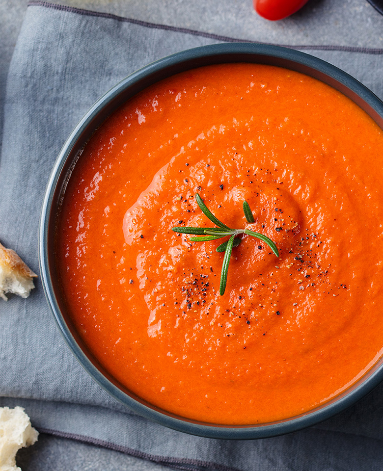 A bowl of creamy tomato soup garnished with rosemary and fresh-cracked pepper. 