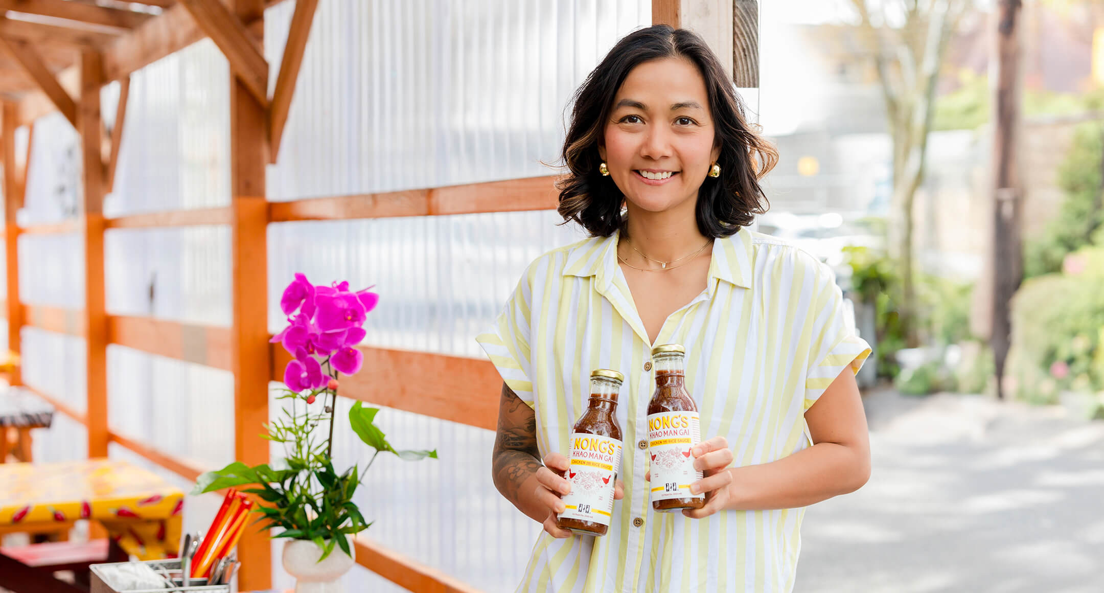 Nong Poonsukwattana, Portland restaurateur holding two bottles of Nong’s Khao Man Gai Sauce.