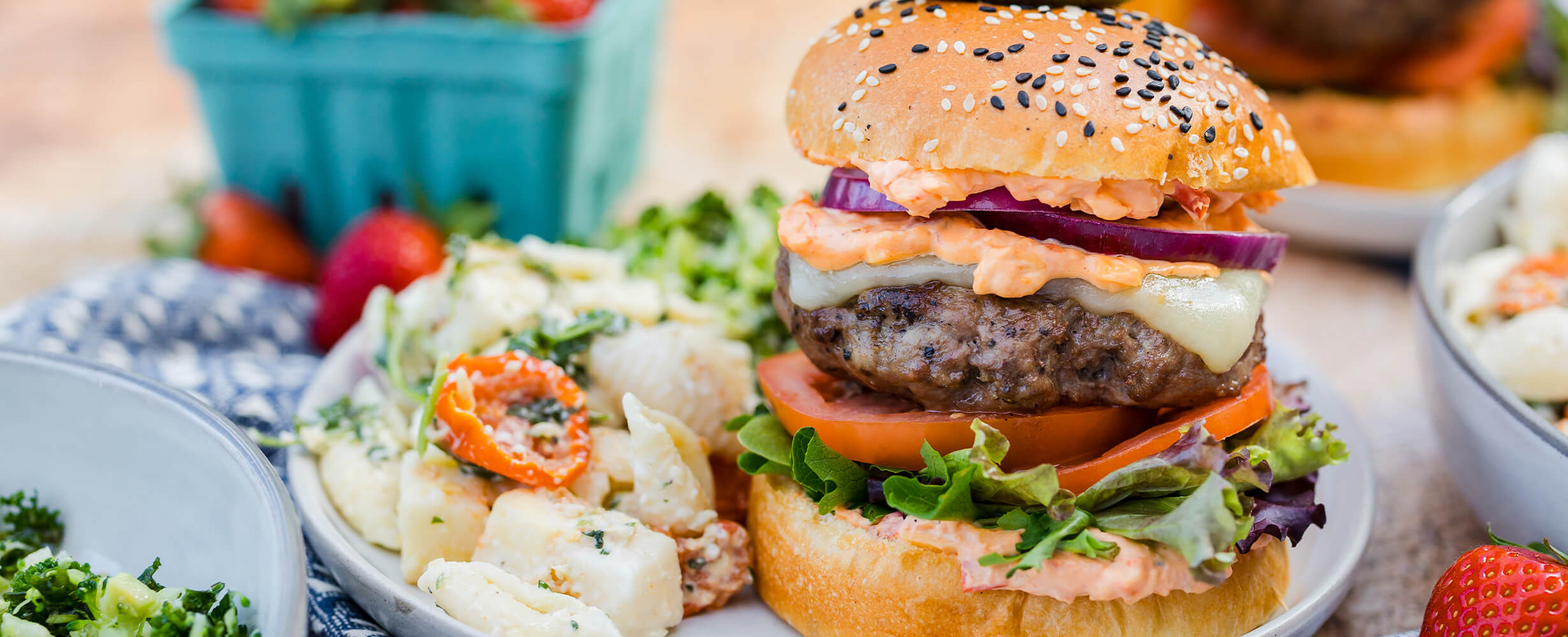 A New Seasons Burger Patty with onion, tomatoes lettuce with a side of pasta salad.