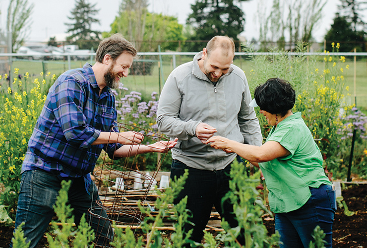 Three people standing together in a community garden.