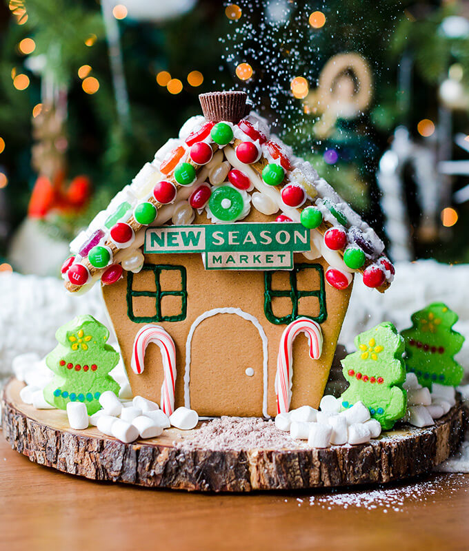a festive decorated gingerbread house with the new seasons market logo on it