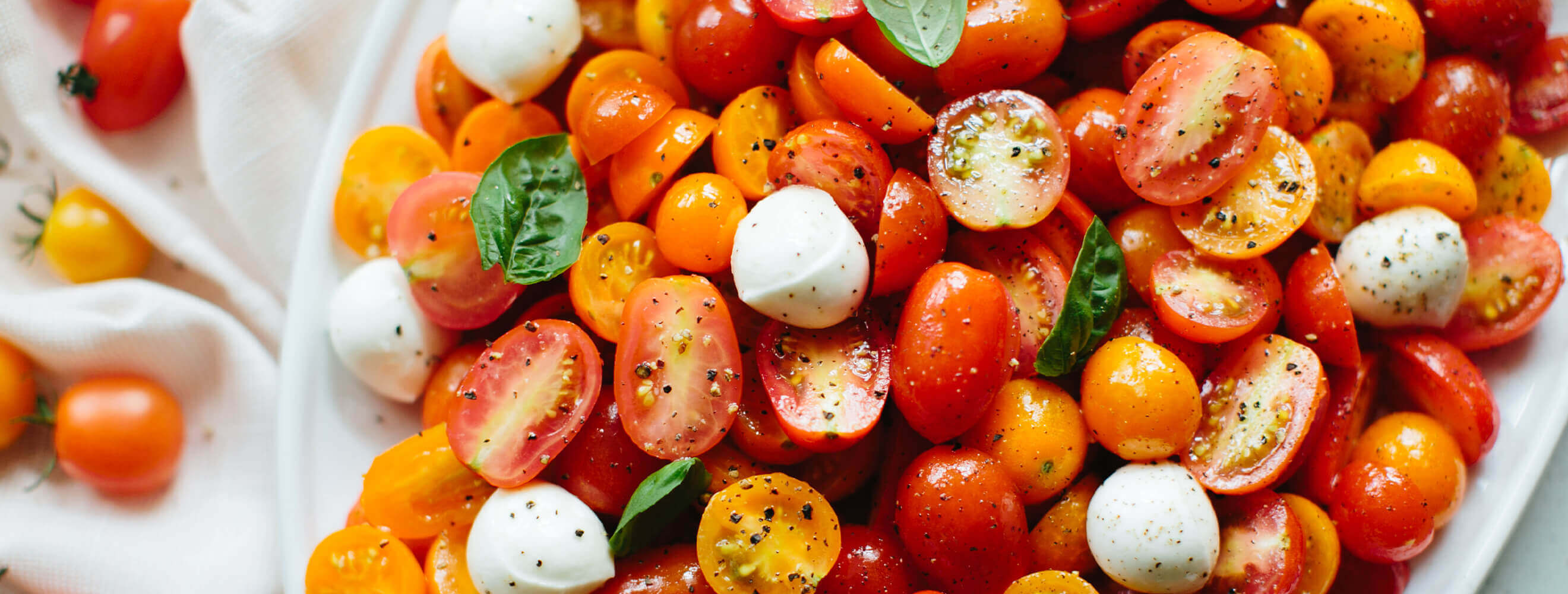 halved cherry tomatoes in orange and red in a serving dish with mozzarella balls and basil.