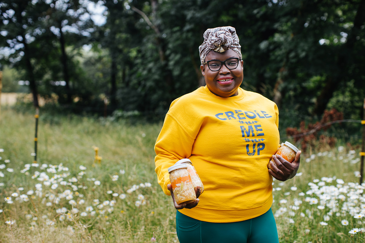 Elsy of Creole Me Up showing off her product in jars, smiling and in a yellow shirt.