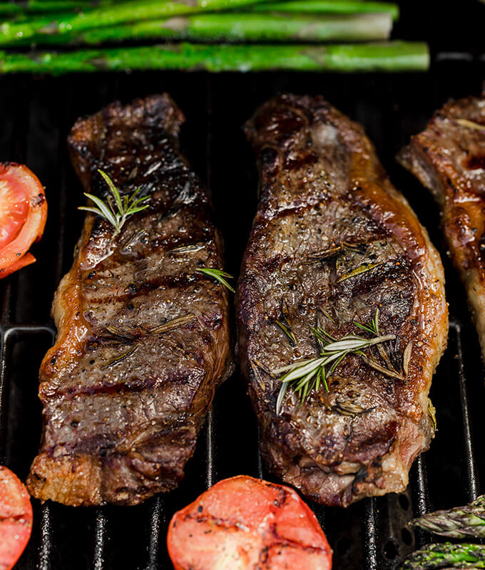 cooked steaks, asparagus and shrimp on a grill grate.
