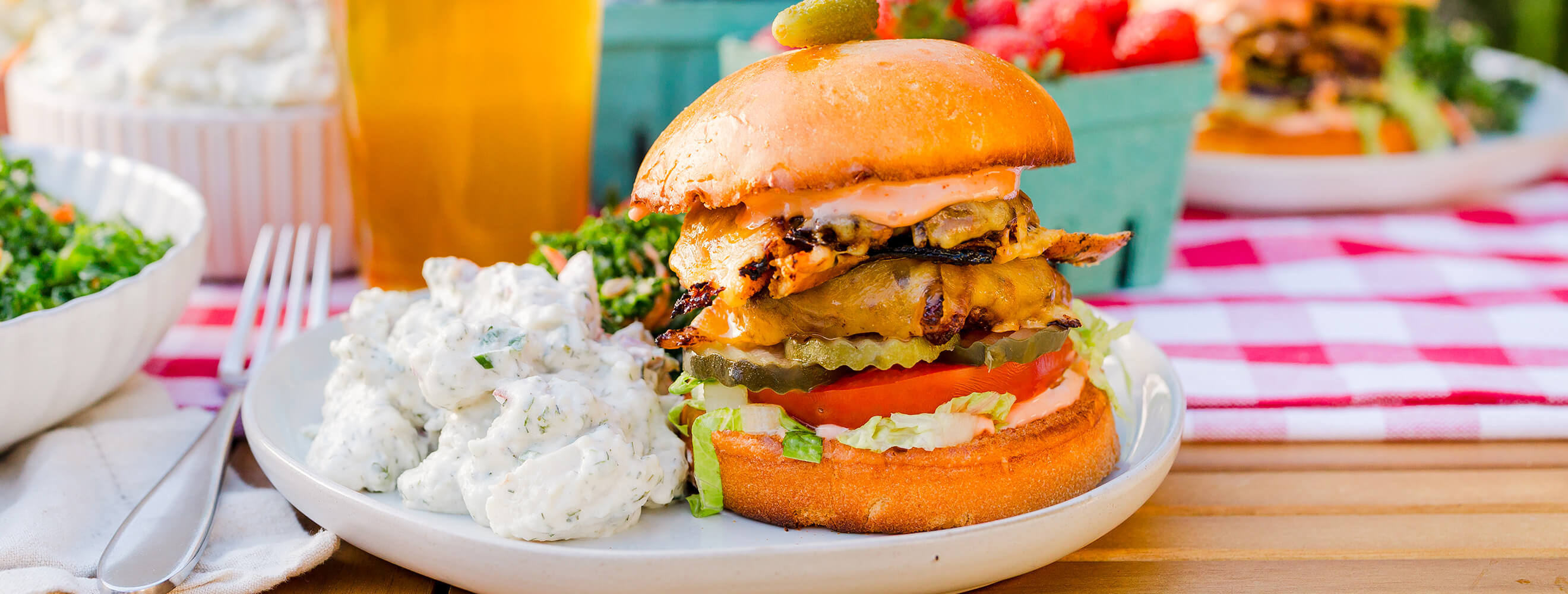 a picnic scene featuring a burger on a bun with cheese and vegetables, and a side of potato salad