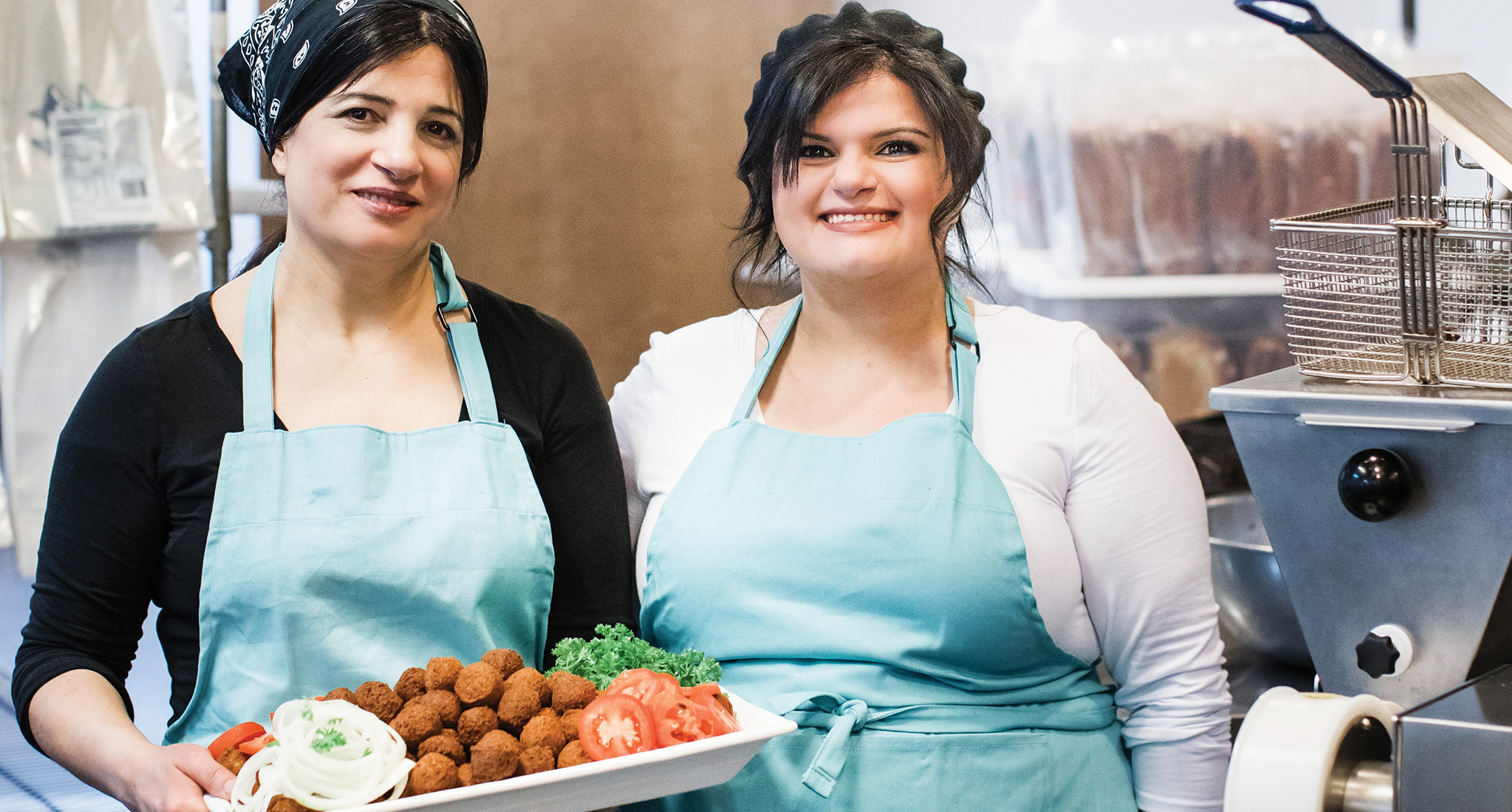 Azeh's Kitchen in blue aprons holding a platter of falafel.