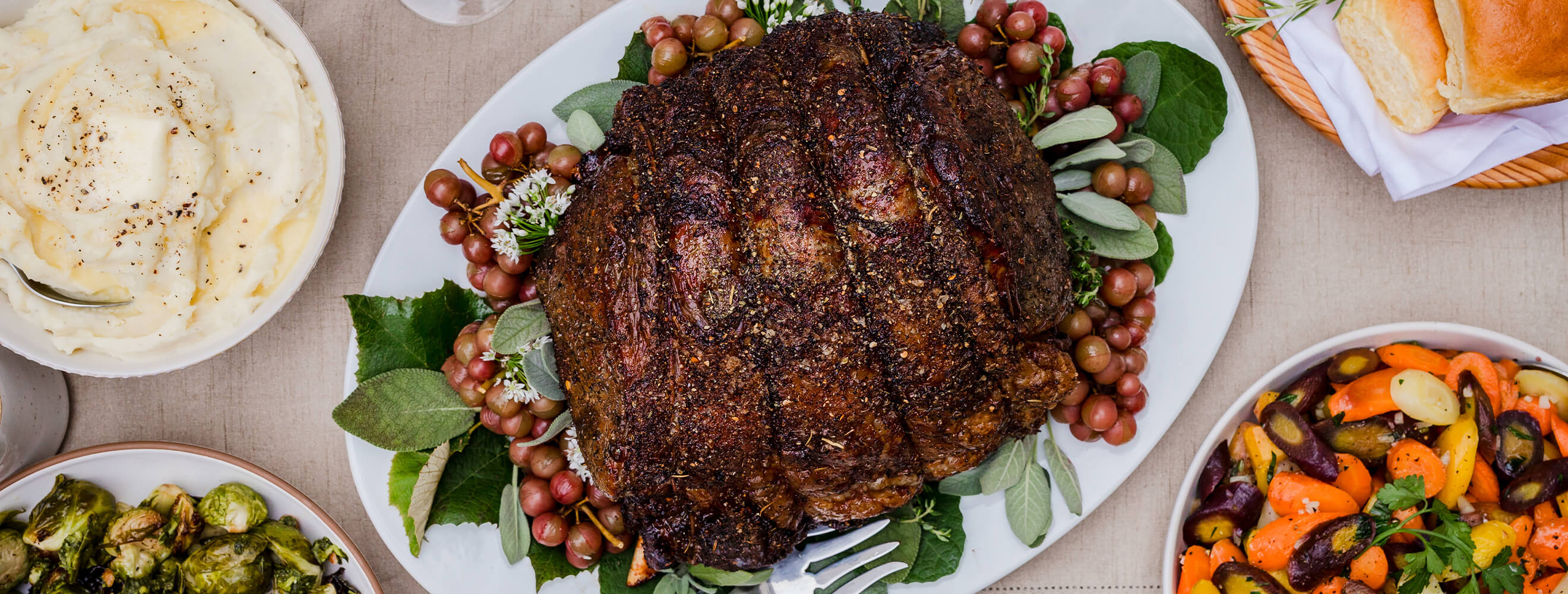 A rib roast on a platter arranged with sides like carrots, rolls and mashed patatoes.