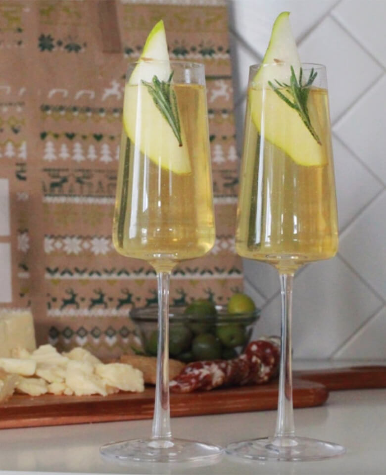 Two glasses of ginger pear cocktail garnished with a slide of pear and a sprig of rosemary.
