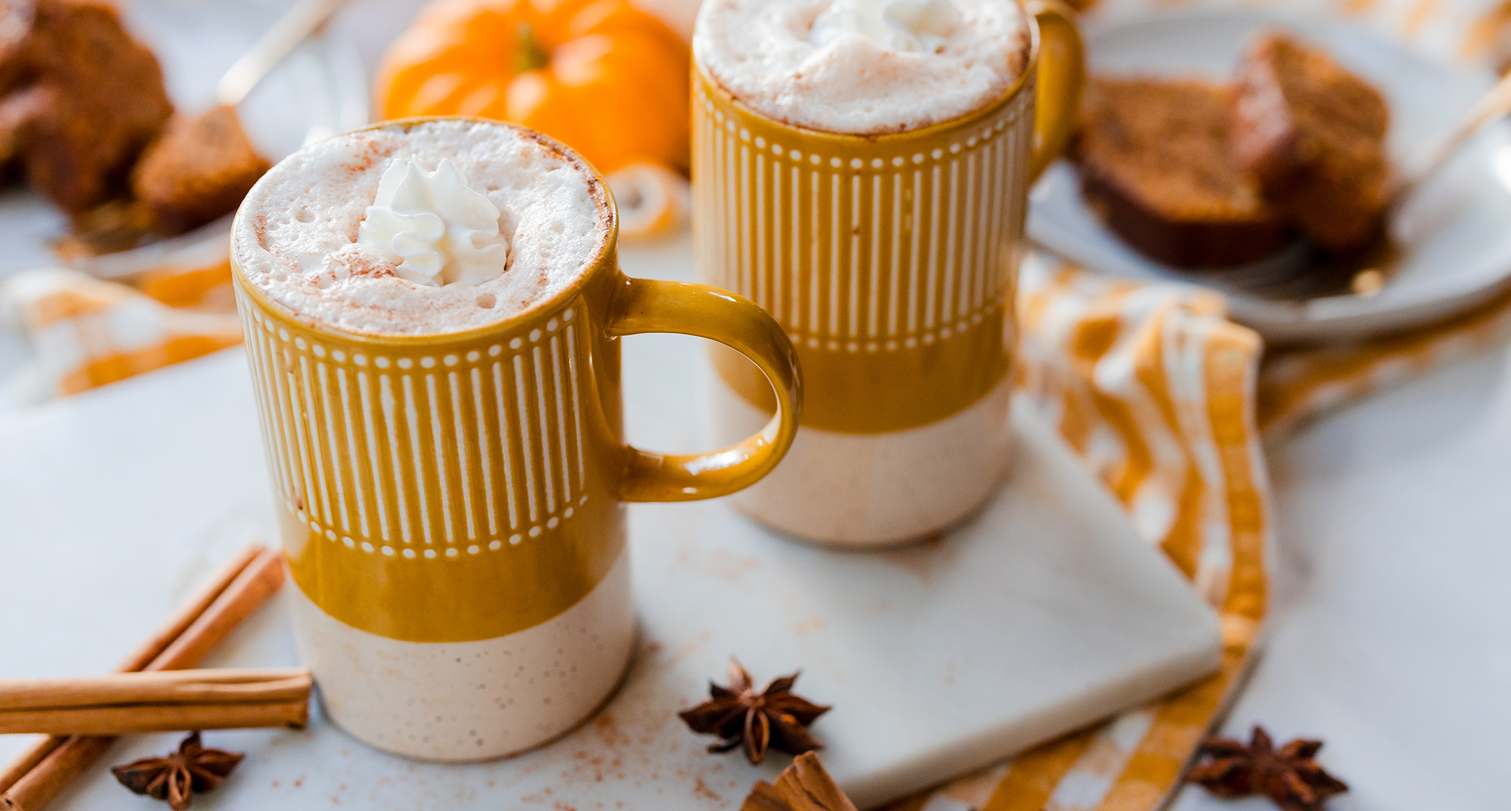 Spiced pumpkin chai in mugs with whipped topping and cinnamon sticks.