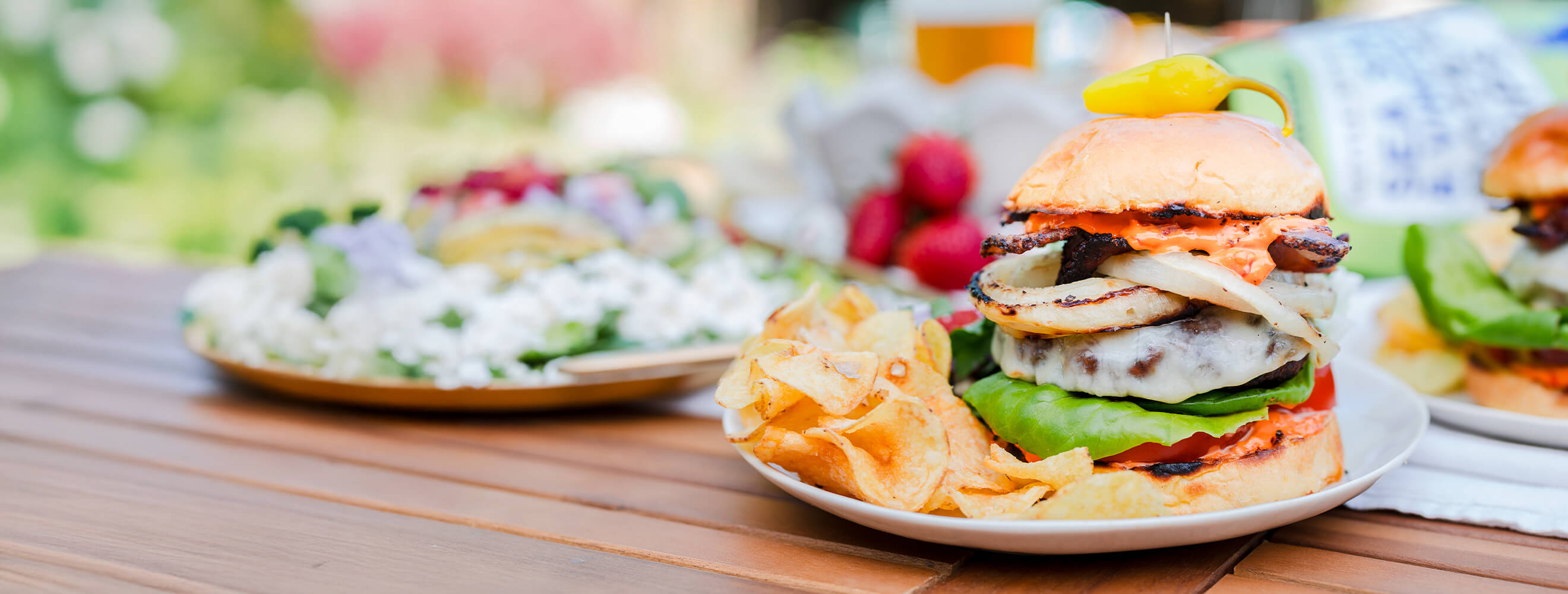 a burger with grilled onions, lettuce, tomato, cheese, bacon and calabrian chili mayo on a plate with chips and salad