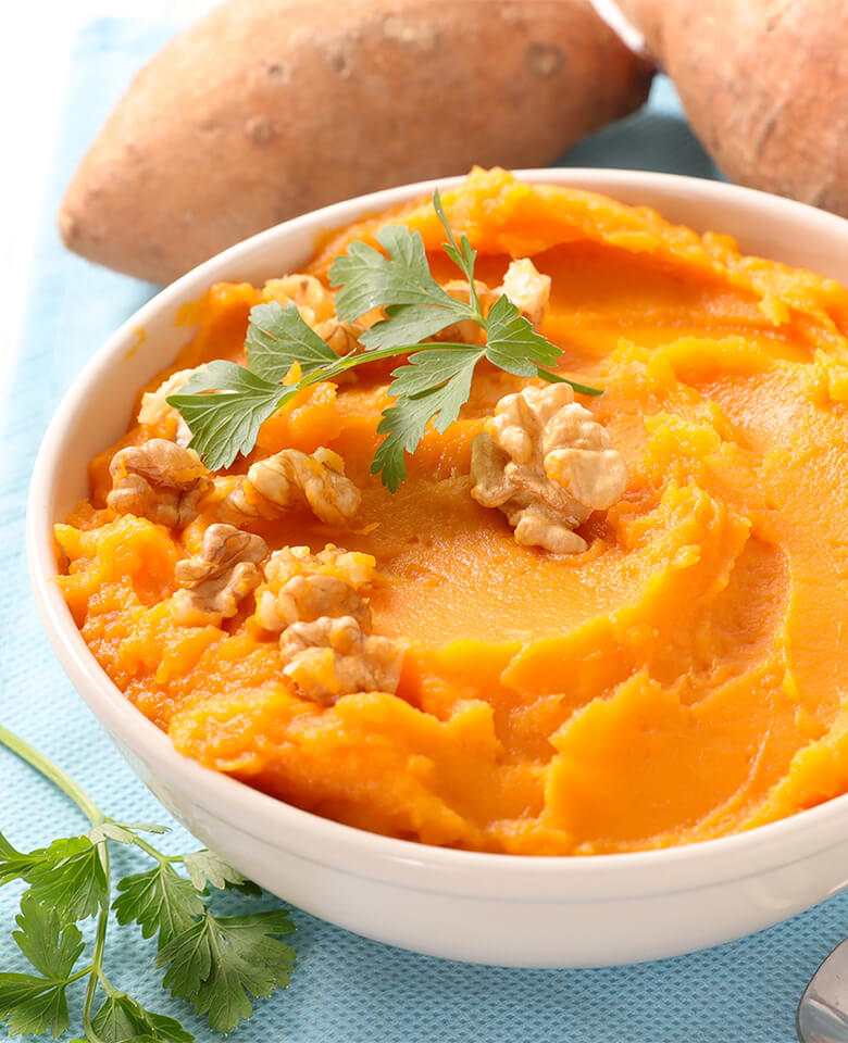 A bowl of mashed sweet potatoes garnished with walnuts
