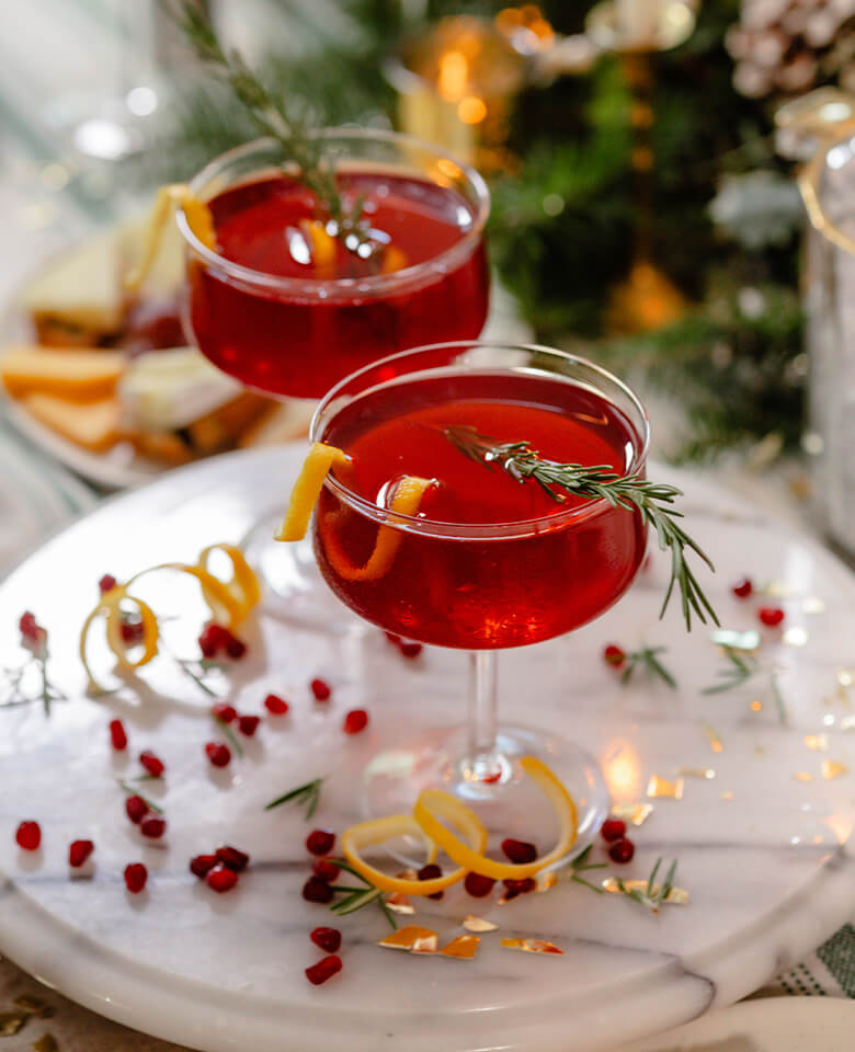 Two glasses of pomegranate French 75 garnished with a sprig of rosemary and a lemon twist.