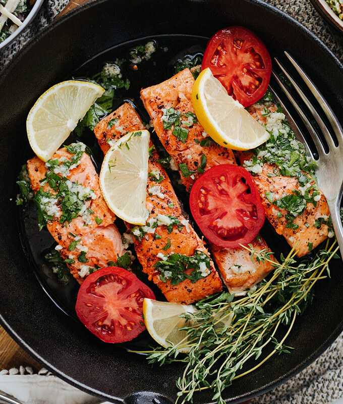 filets of salmon on a grill with herbs and sliced lemon and tomato