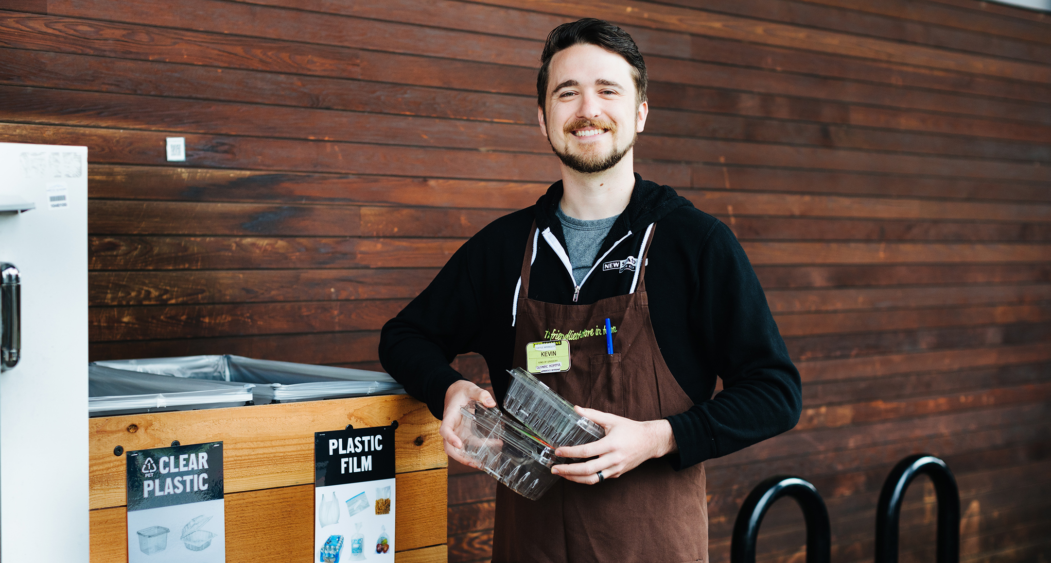 Staff member holding plastic recyclables near drop off bins.