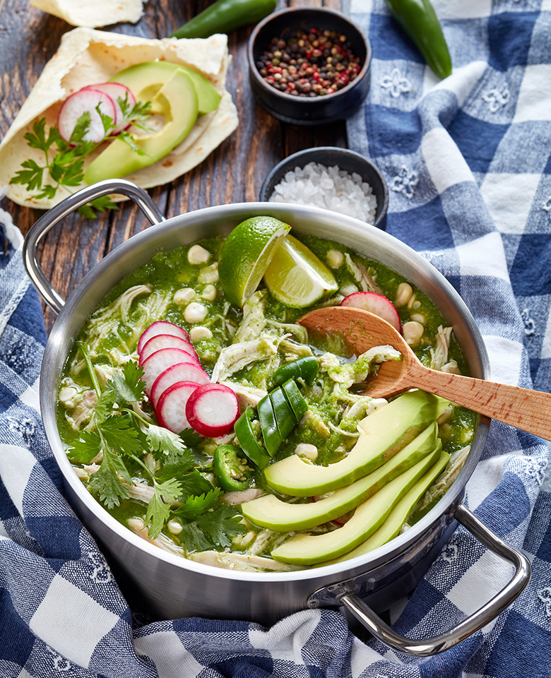 a bowl of chicken verde soup topped with avocado, radishes and cilantro.