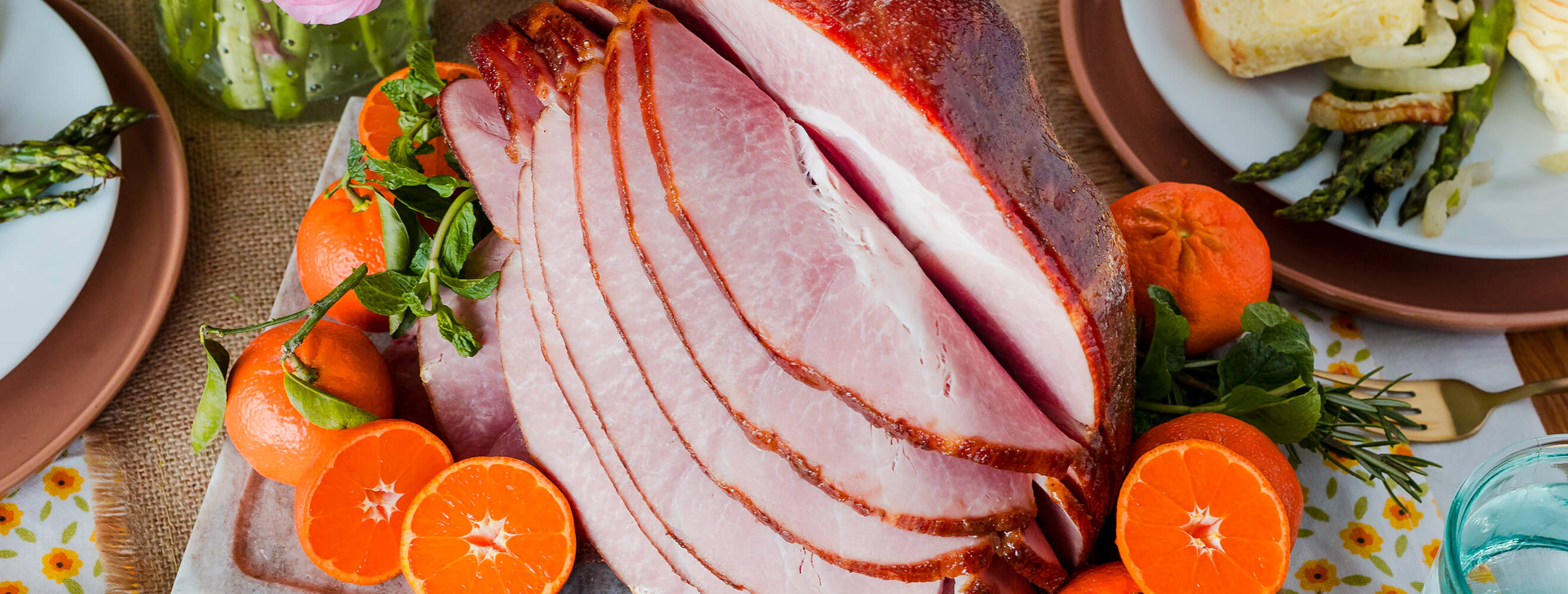 a spiral sliced holiday ham shot from above and surrounded with cut oranges.