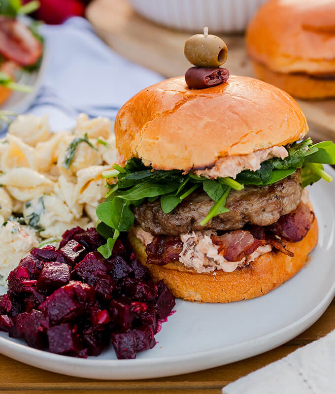 a burger with a bun on a plate with beets and a pasta salad.