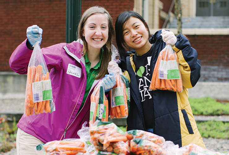 Two people holding bags of carrots as part of a volunteer group.
