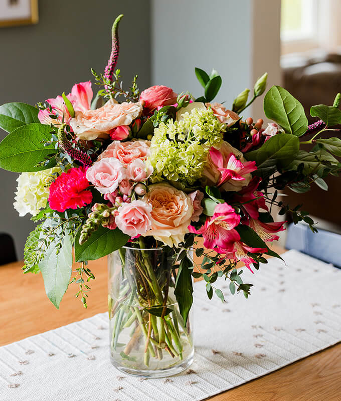 a floral bouquet in a vase on a table with a tablecloth.