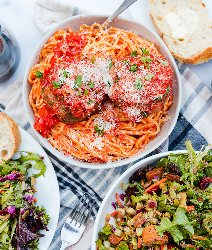 An overhead shot of a bowl of spaghetti and meatballs with salad and bread on the side.